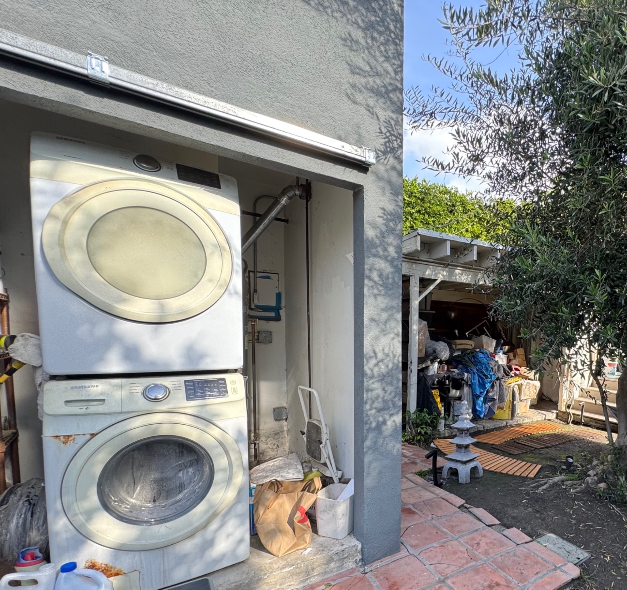Inspection-week photograph showing the stacked washer and dryer, blue tape on the electrical area, and surrounding stored items